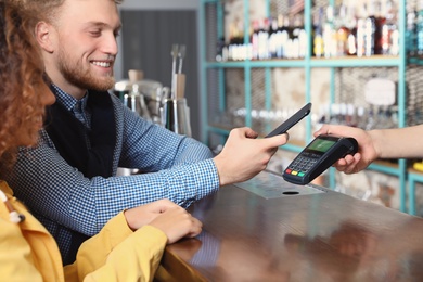 Clients using smartphone and credit card machine for non cash payment in cafe