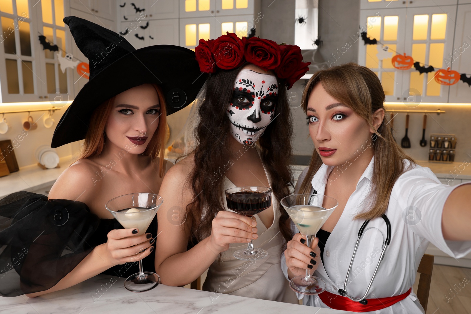 Photo of Group of women in scary costumes with cocktails taking selfie at Halloween party indoors