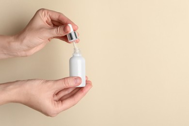 Photo of Woman with bottle of cosmetic serum and dropper on beige background, closeup. Space for text