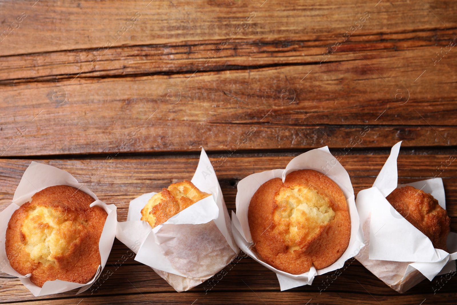 Photo of Delicious sweet muffins on wooden table, flat lay. Space for text