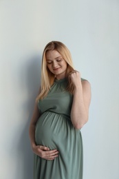 Young pregnant woman touching belly on light background