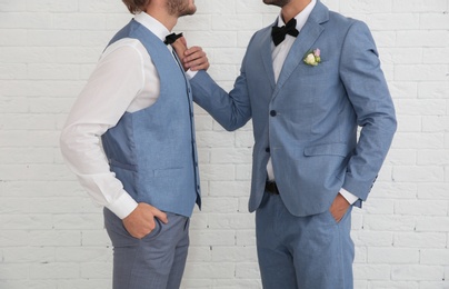 Photo of Newlywed gay couple near white brick wall, closeup