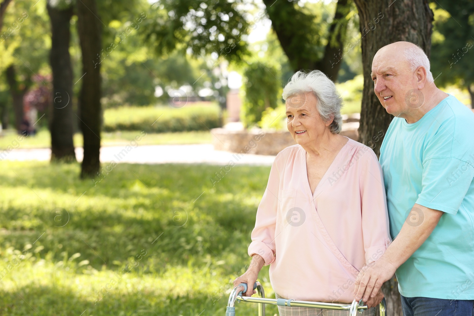 Photo of Elderly man helping his wife with walking frame outdoors