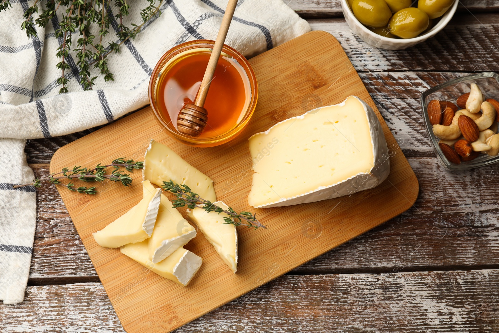 Photo of Tasty Camembert cheese with thyme, honey and nuts on wooden table, flat lay