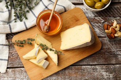 Tasty Camembert cheese with thyme, honey and nuts on wooden table, flat lay