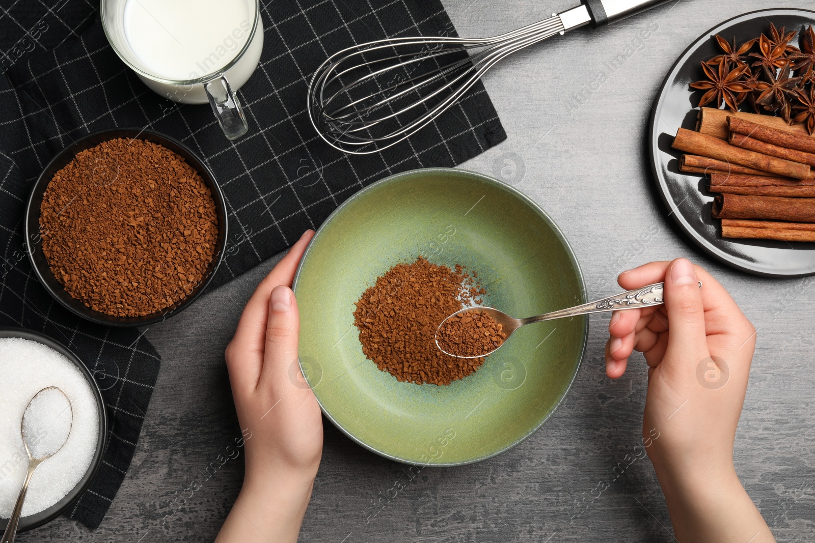 Photo of Making dalgona coffee. Woman pouring instant granules into bowl at gray table, top view