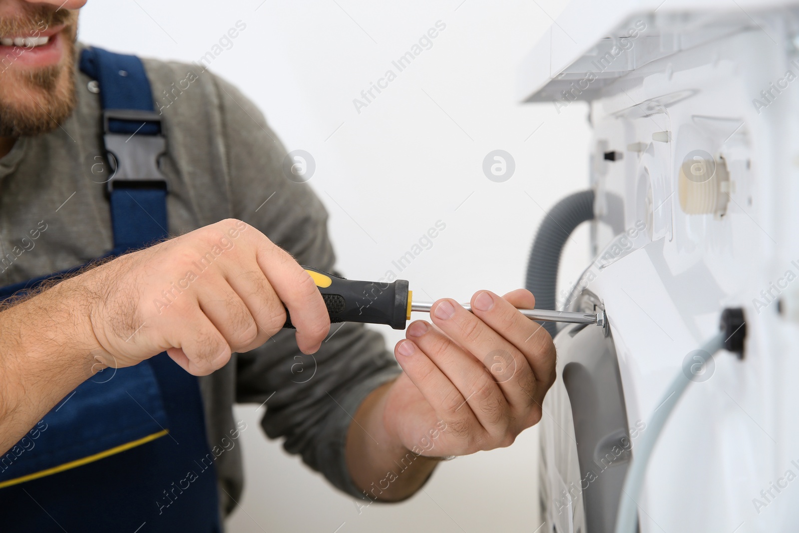 Photo of Young plumber fixing washing machine in bathroom, closeup