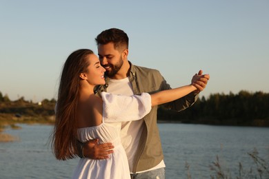 Beautiful couple dancing near river at sunset