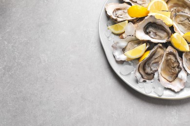 Photo of Fresh oysters with lemon and ice on grey table, top view. Space for text
