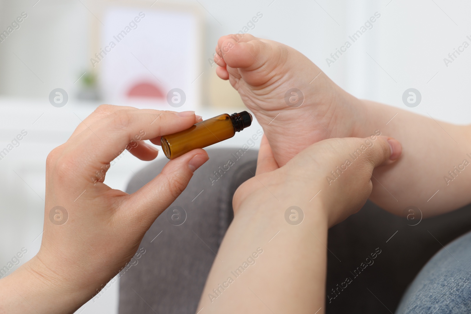 Photo of Mother applying essential oil from roller bottle onto her baby`s heel indoors, closeup