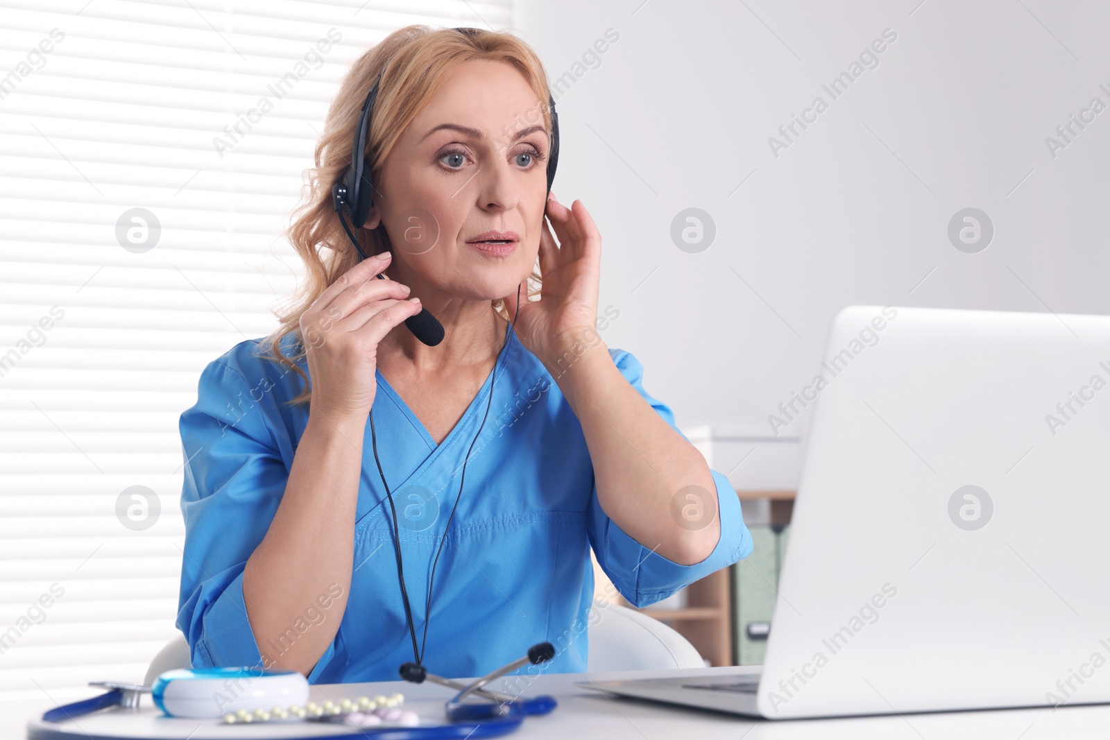 Photo of Doctor with laptop and headphones consulting patient in clinic. Online medicine concept