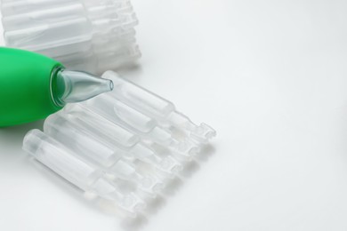 Single dose ampoules of sterile isotonic sea water solution and nasal aspirator on white background, closeup. Space for text