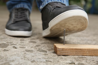 Photo of Careless man stepping on nail in wooden plank outdoors, closeup