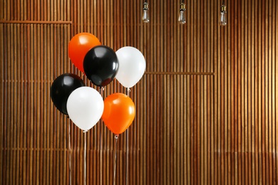 Photo of Colorful balloons against wooden wall, space for text. Halloween party
