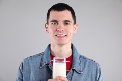 Happy man with milk mustache holding glass of tasty dairy drink on gray background