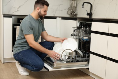 Smiling man loading dishwasher with plates in kitchen