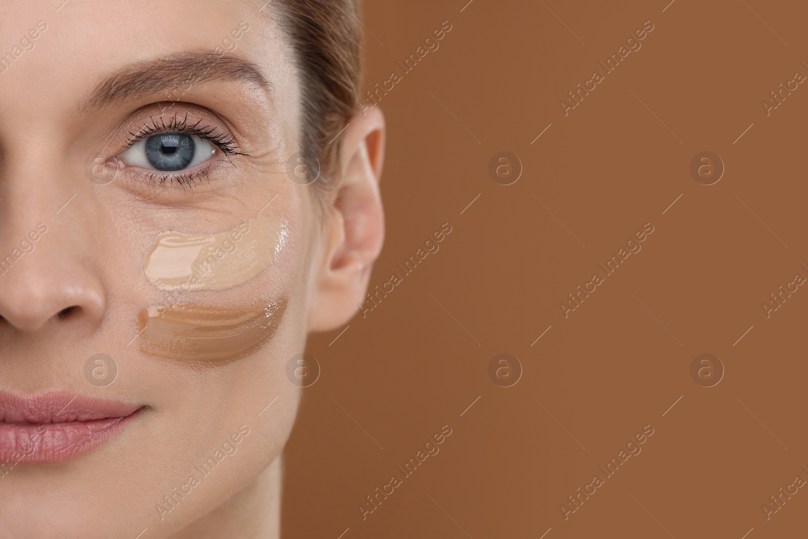 Photo of Woman with swatches of foundation on face against brown background, closeup. Space for text