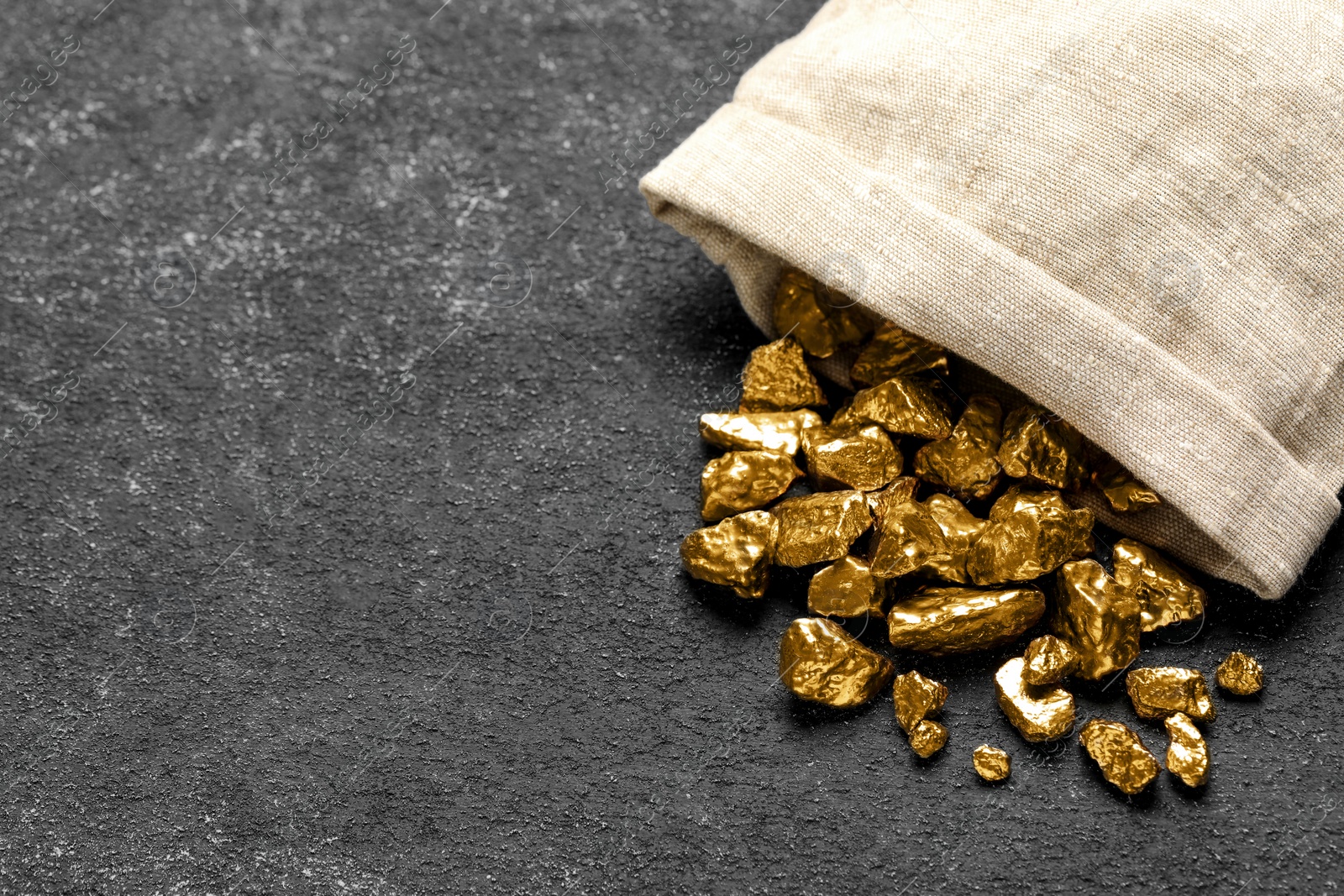 Photo of Overturned sack of gold nuggets on grey table. Space for text