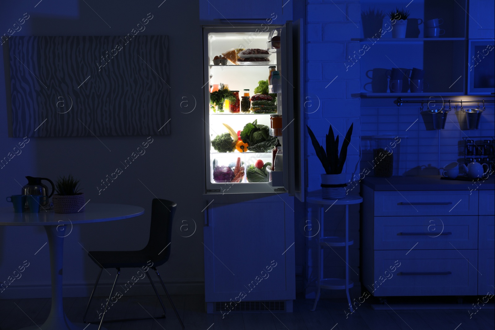 Photo of Open refrigerator full of products in stylish kitchen interior at night