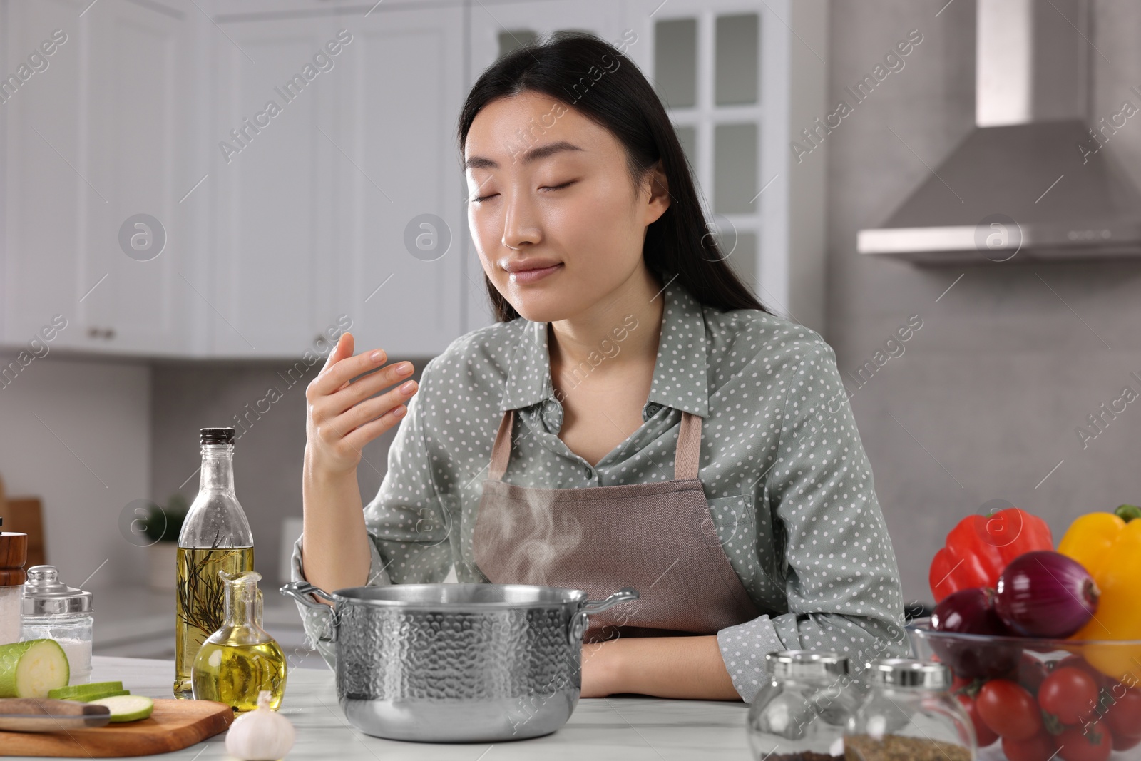 Photo of Beautiful woman smelling soup after cooking at countertop in kitchen