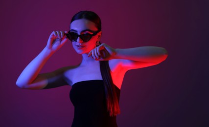 Portrait of beautiful young woman in sunglasses on color background with neon lights