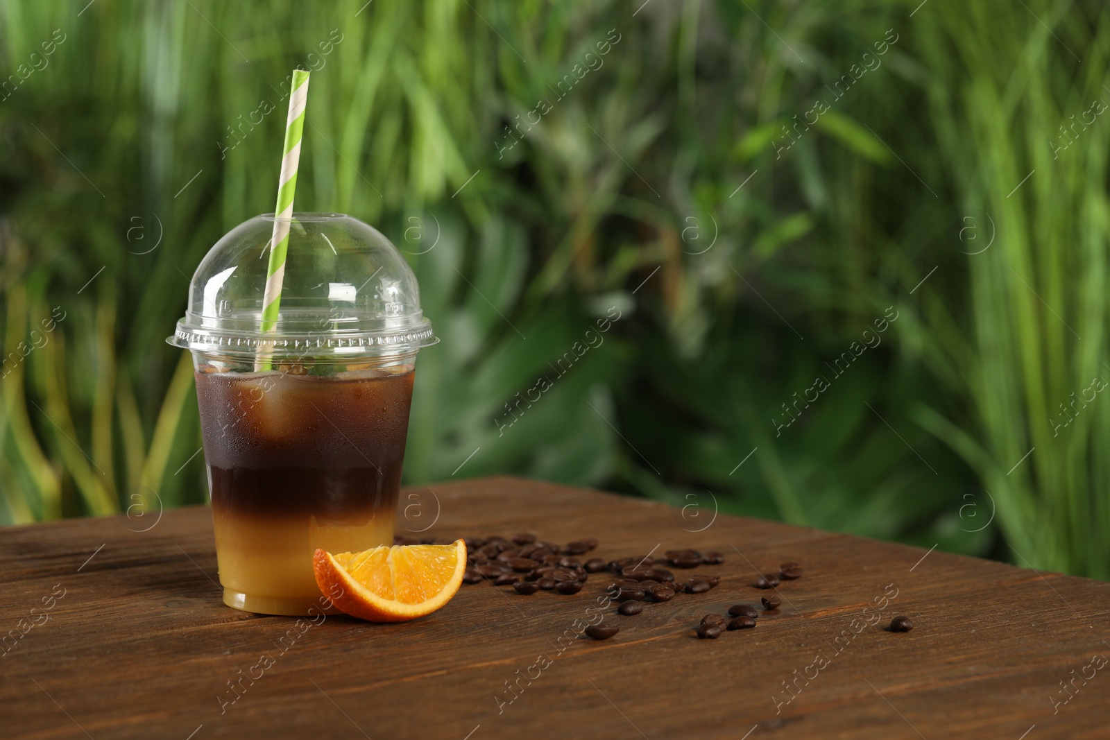 Photo of Tasty refreshing drink with coffee and orange juice in plastic cup on wooden table against blurred background, space for text