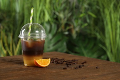 Photo of Tasty refreshing drink with coffee and orange juice in plastic cup on wooden table against blurred background, space for text