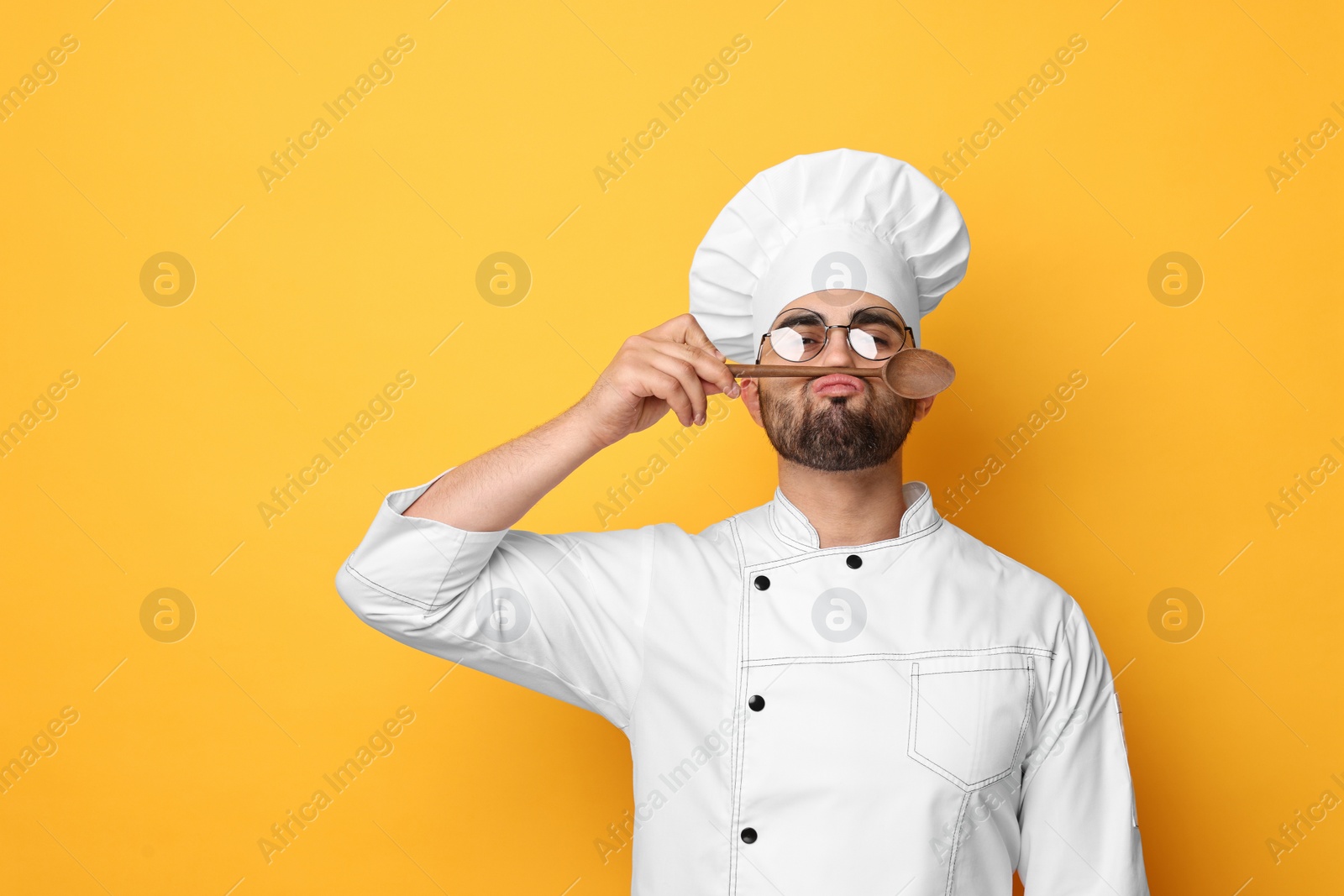 Photo of Professional chef with wooden spoon having fun on yellow background. Space for text