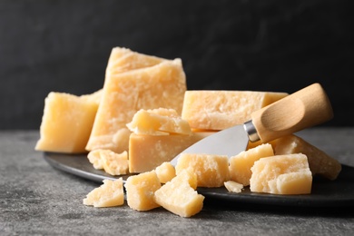 Photo of Parmesan cheese with board and knife on grey table, closeup