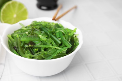 Photo of Tasty seaweed salad in bowl on white tiled table, closeup