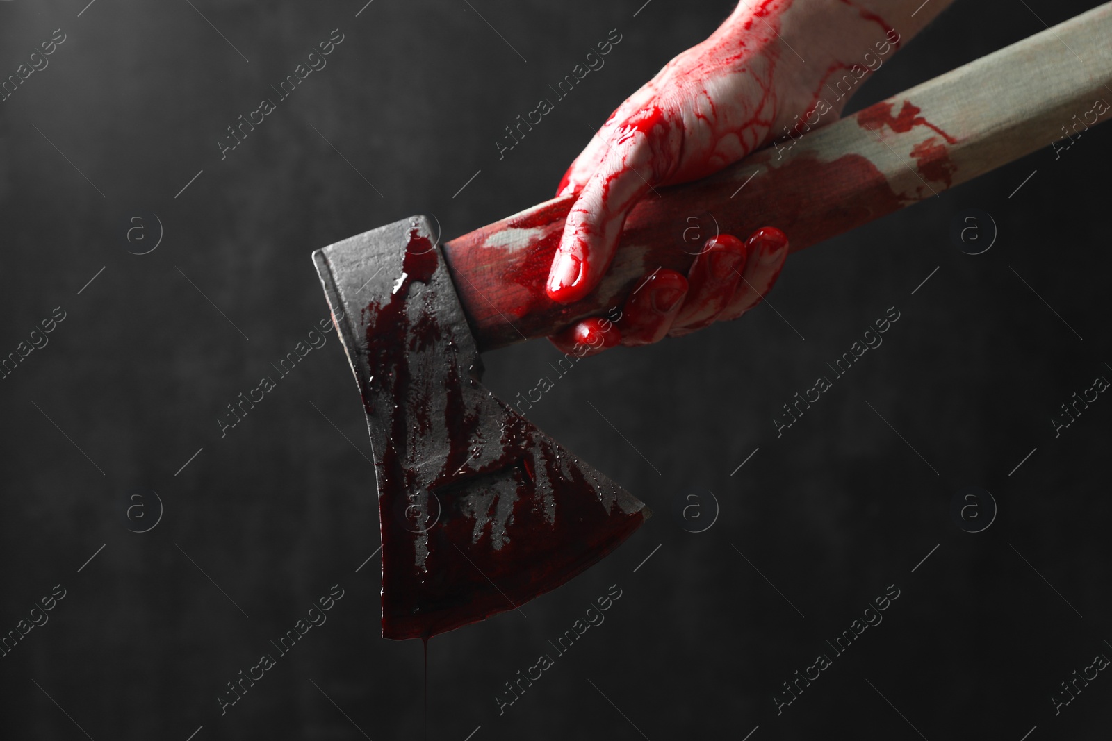 Photo of Man holding bloody axe on dark gray background, closeup