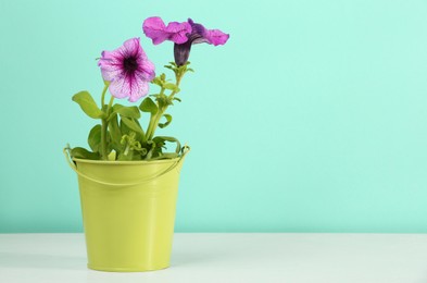Photo of Beautiful petunia flowers in green pot on wooden table against turquoise background. Space for text