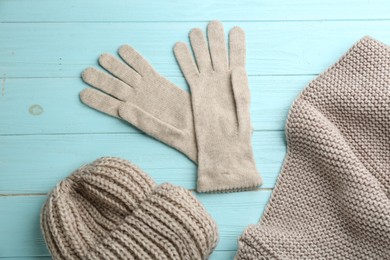 Stylish gloves, scarf and hat on light blue wooden background, flat lay