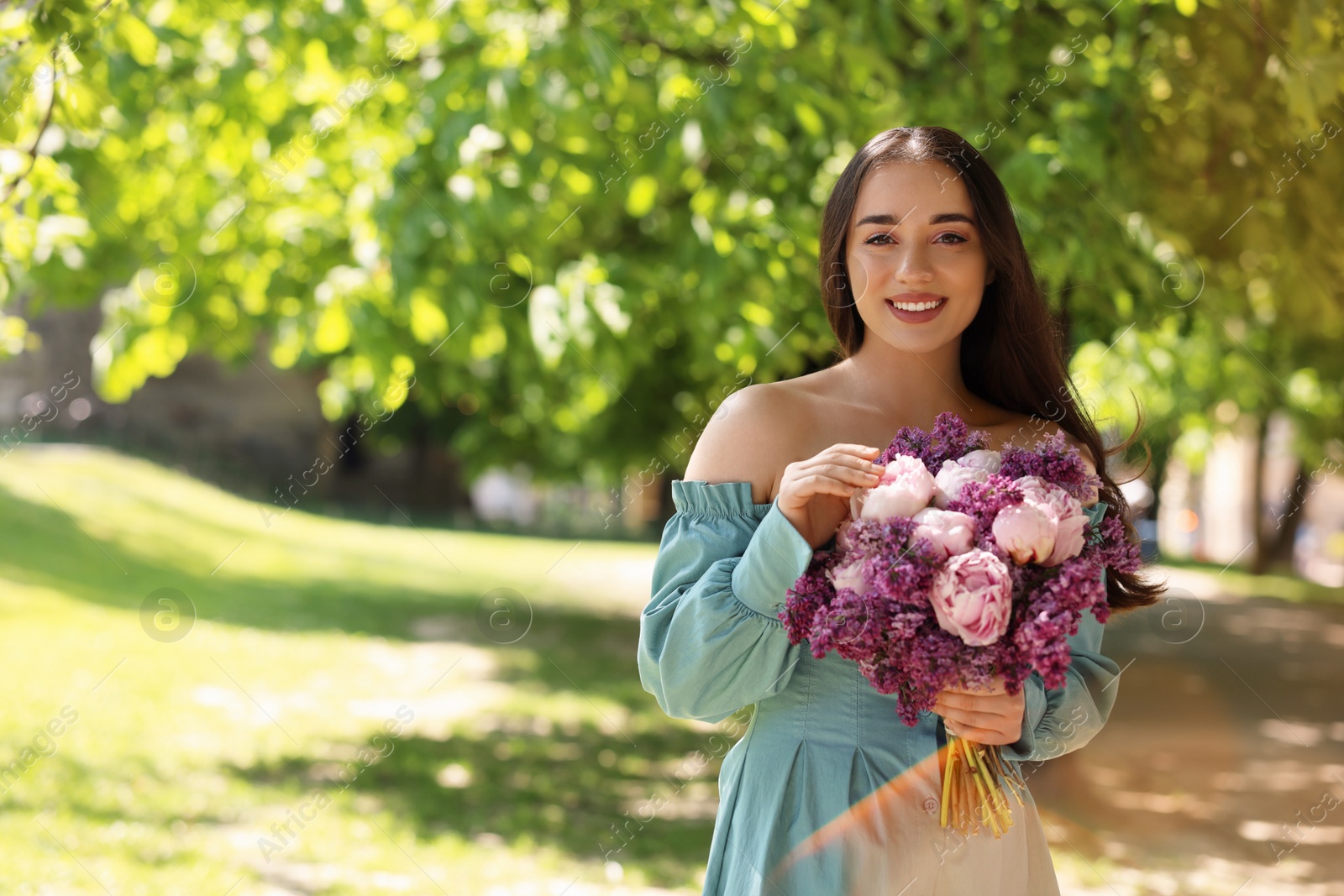 Photo of Beautiful woman with bouquet of spring flowers in park on sunny day, space for text