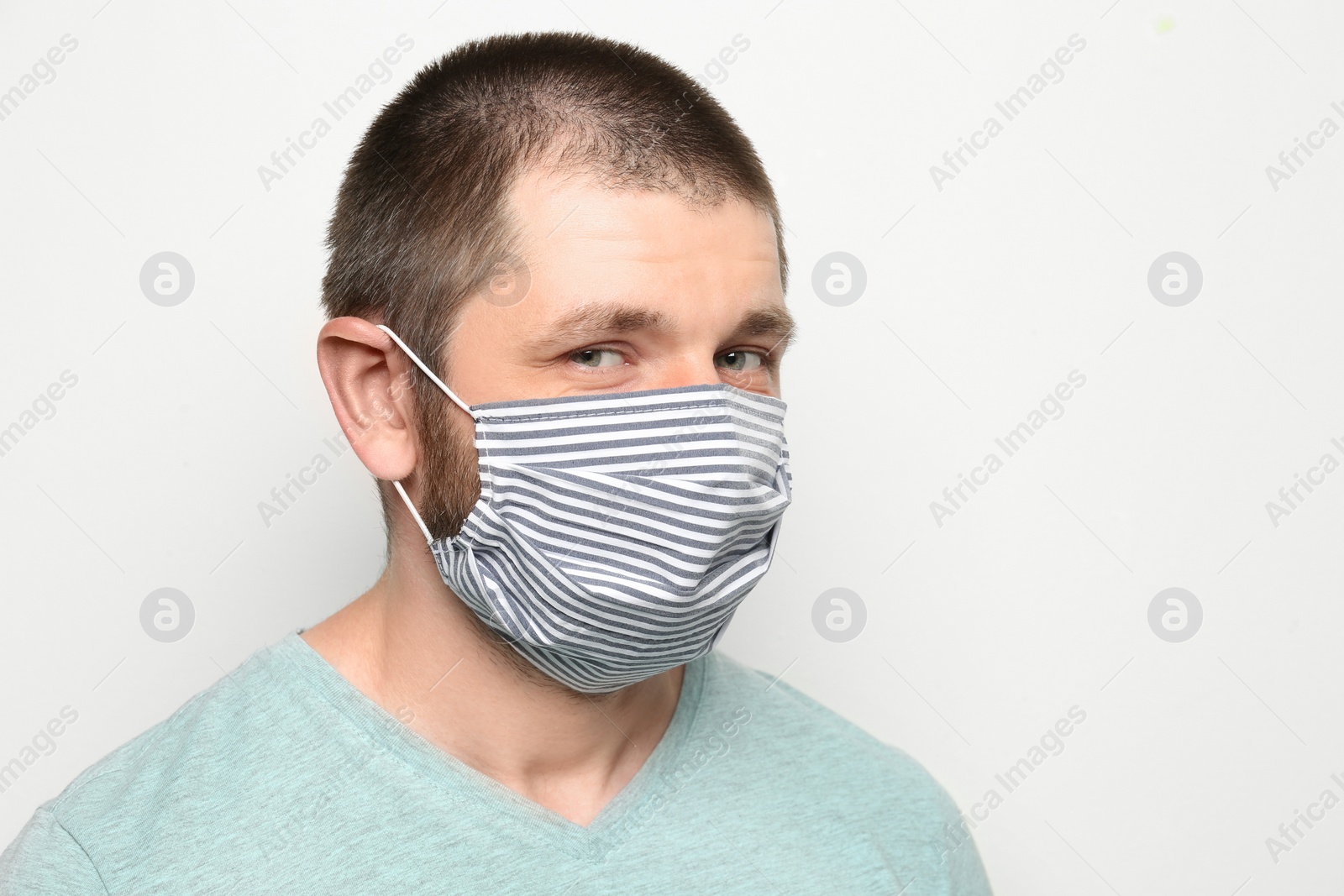 Photo of Man wearing handmade cloth mask on white background, space for text. Personal protective equipment during COVID-19 pandemic