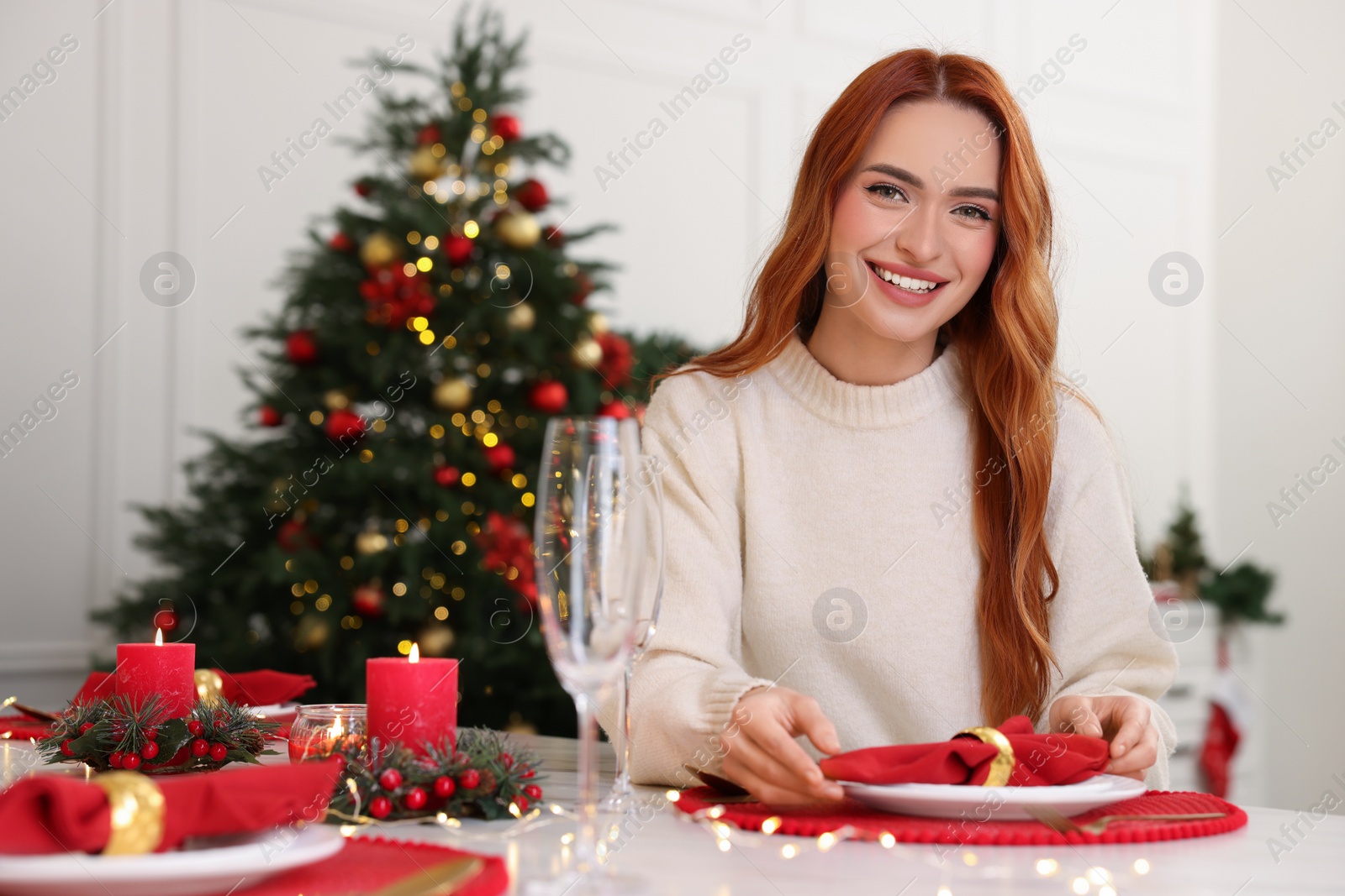 Photo of Beautiful young woman setting table in room decorated for Christmas