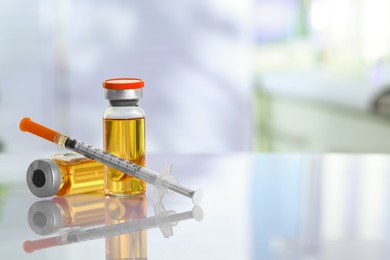 Photo of Glass vials and syringe with orange medication on white table. Space for text
