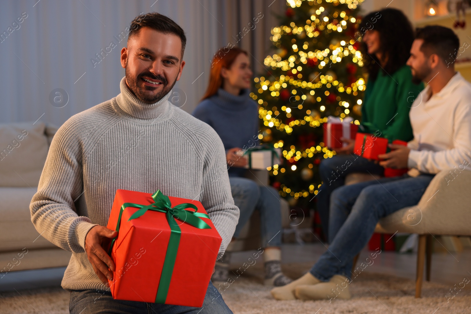 Photo of Christmas celebration in circle of friends. Happy man with gift box at home, selective focus