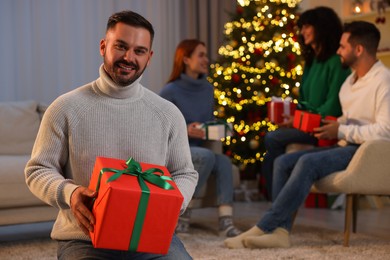 Photo of Christmas celebration in circlefriends. Happy man with gift box at home, selective focus