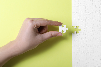 Photo of Woman putting last piece of white puzzle on yellow background, closeup