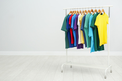 Photo of Rack with colorful t-shirts in room. Space for text