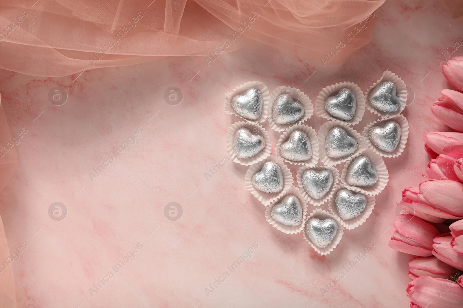 Photo of Heart made with delicious chocolate candies and beautiful tulips on pink table, flat lay. Space for text