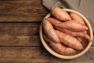 Photo of Fresh whole sweet potatoes in bowl on wooden table, top view. Space for text