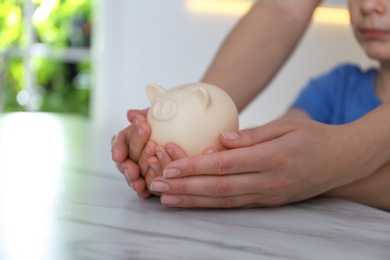 Photo of Mother and son with piggy bank at marble table indoors, closeup