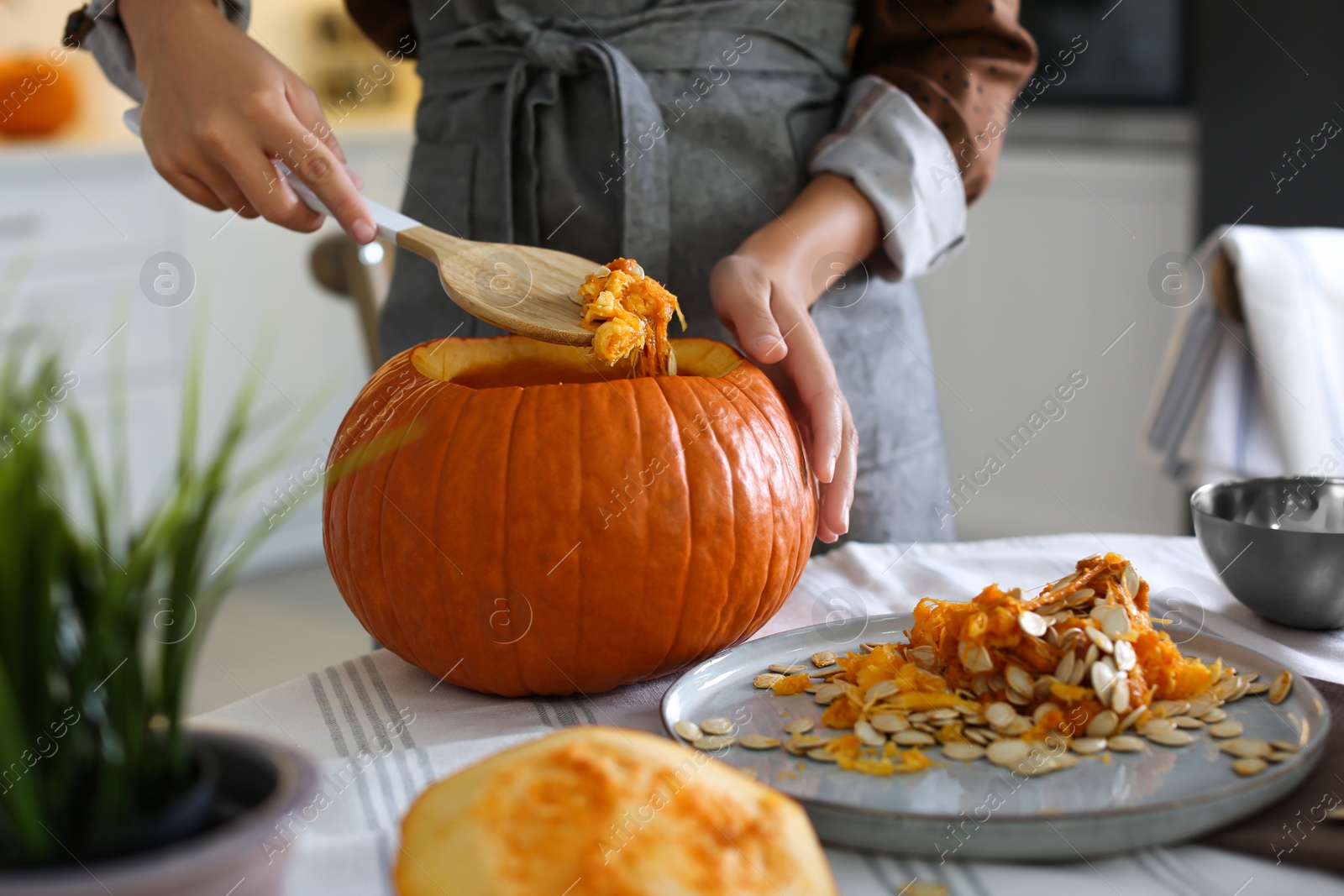 Photo of Woman making pumpkin jack o'lantern at table indoors. Halloween celebration