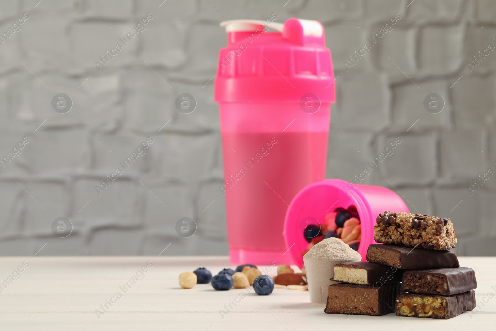 Photo of Different energy bars, nuts, blueberries, protein cocktail and powder on white wooden table. Space for text