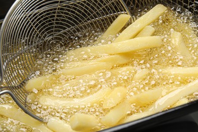 Cooking delicious french fries in hot oil, closeup