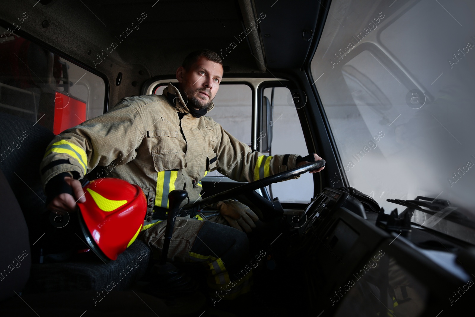 Photo of Firefighter in uniform with helmet driving modern fire truck