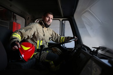 Photo of Firefighter in uniform with helmet driving modern fire truck