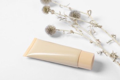 Tube of skin foundation and decorative flowers on white background. Makeup product